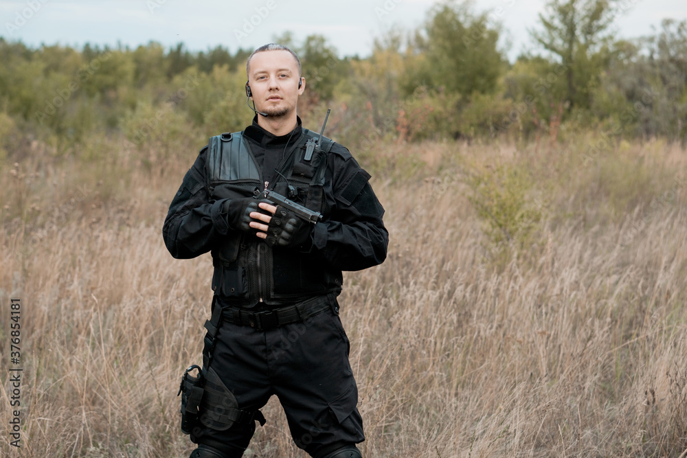 Portrait of special forces soldier in black uniform with a pistol. Copy space.