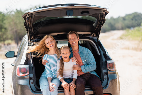 Parents embracing child while sitting in trunk of car during weekend © LIGHTFIELD STUDIOS