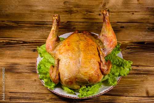 Plate with roasted whole chicken and lettuce leaves on a wooden table