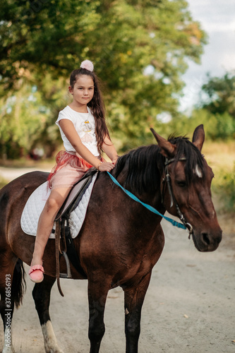 Little blonde girl with long hair rides a horse in the park at sunset in autumn. Autumn horse ride. Friendship of a girl and a horse. © sergo321
