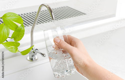 Hand pouring a glass of water from kitchen filter tap
