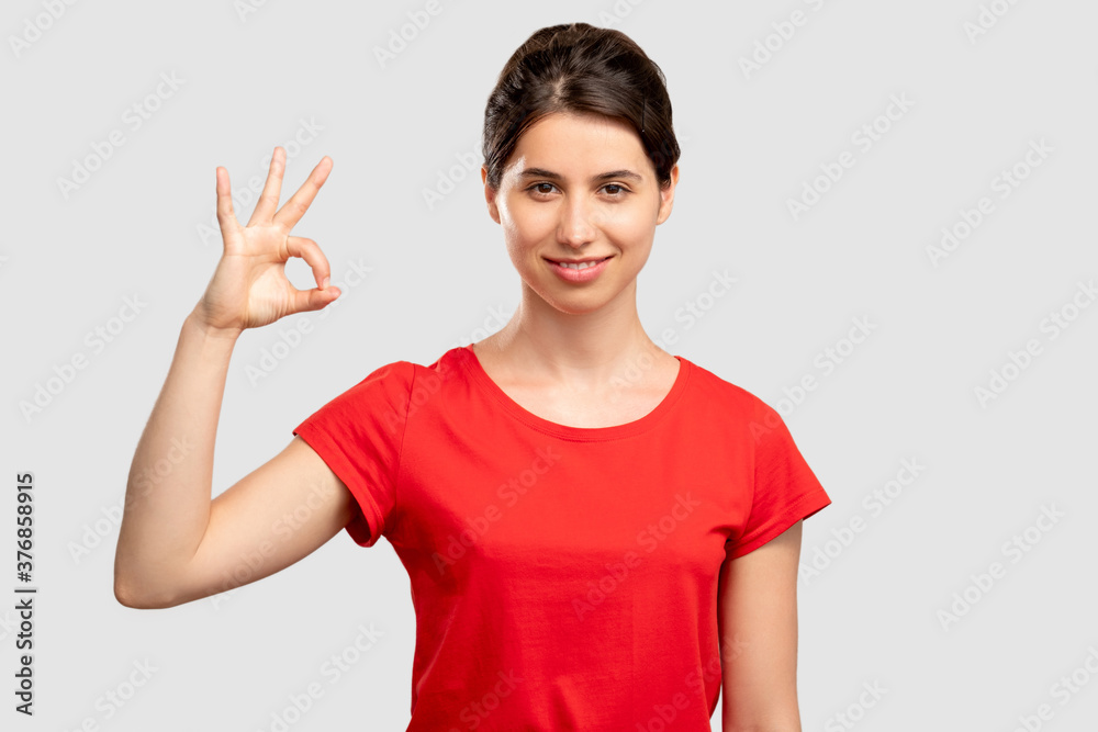 Ok gesture. Approval sign. Happy young in red t-shirt woman showing fine looking at camera isolated on neutral. Good job. Positive lifestyle. Advertising background Ok gesture. Approval sign. Happy young in red t-shirt woman showing fine looking at camera isolated on neutral. Good job. Positive lifestyle. Advertising background