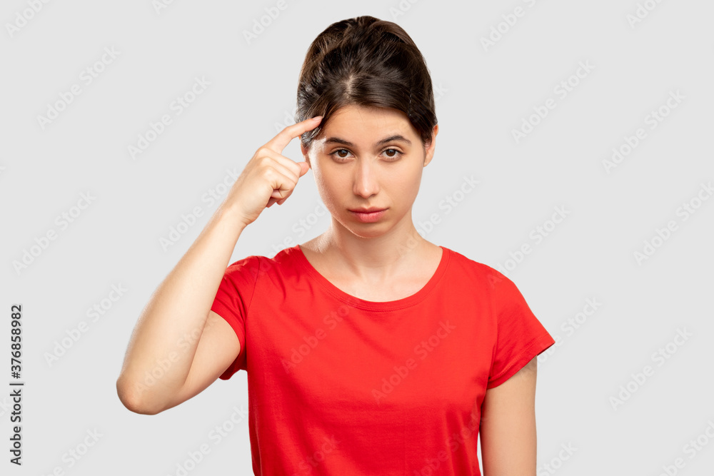 Silly idea. Stupid gesture. Doubtful woman holding finger on head. Looking at camera isolated on neutral copy space. Cuckoo sign. Displeased blaming. Critical attitude Silly idea. Stupid gesture. Doubtful woman holding finger on head. Looking at camera isolated on neutral copy space. Cuckoo sign. Displeased blaming. Critical attitude