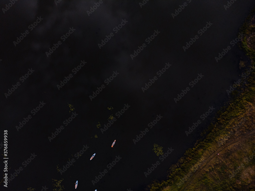 Obraz premium Top view of tourists on lake with SUP-boards. Beautiful clear water with people floating on boards engaged in sup-surfing. Seascape with people rowing on boards on background horizon