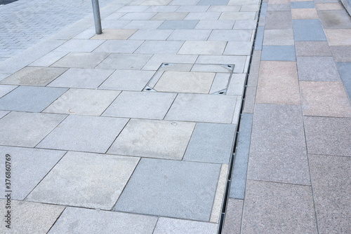 Cast iron rain or anover metal stormwater drainage system a downspout and slit tray with garbage on urban street paving walkway