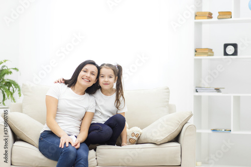 Photo of mother and her cute daughter posing on white sofa. © Andrii