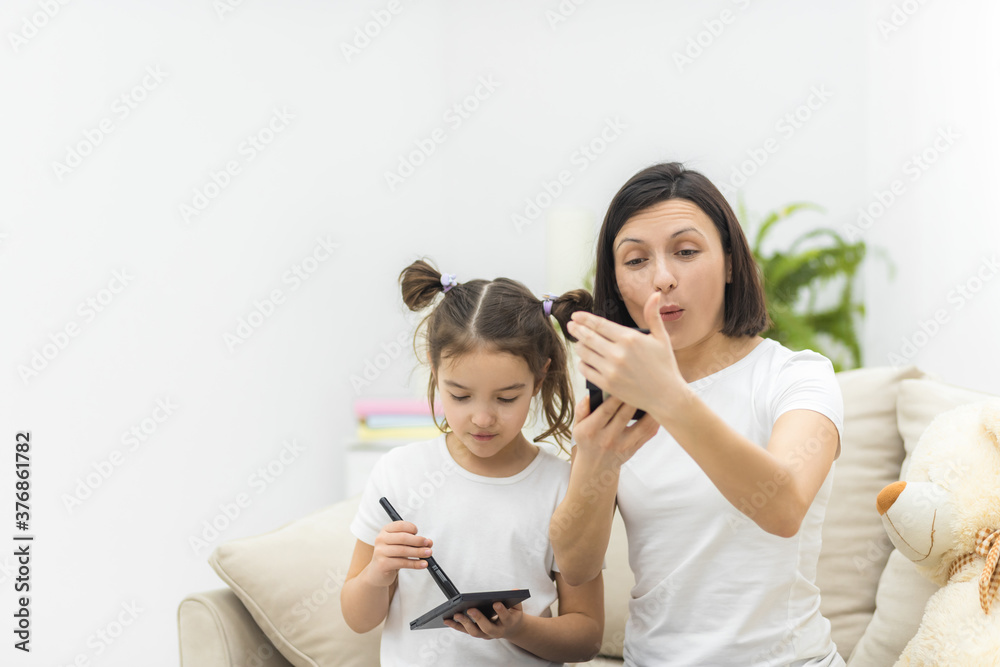 Photo of little daughter helping her young mother with the make up.