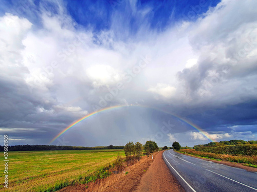 the phenomenon of a hemispherical rainbow in a natural landscape, fields, forests, road. the colorful spectacle of the appearance of a rainbow in late summer, autumn