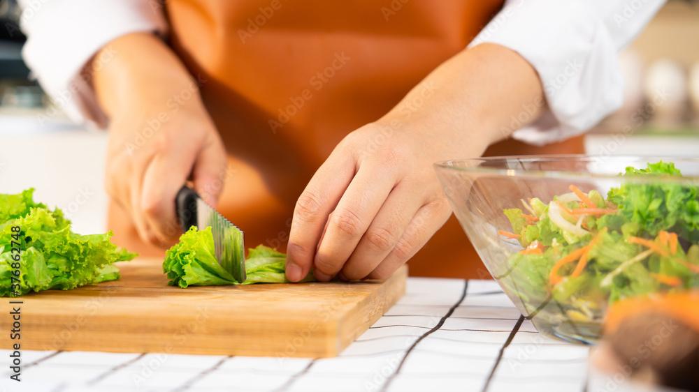 young Asian woman is preparing healthy food vegetable salad by Cutting ingredients on cutting board on light kitchen, Cooking At Home and healthy food concept