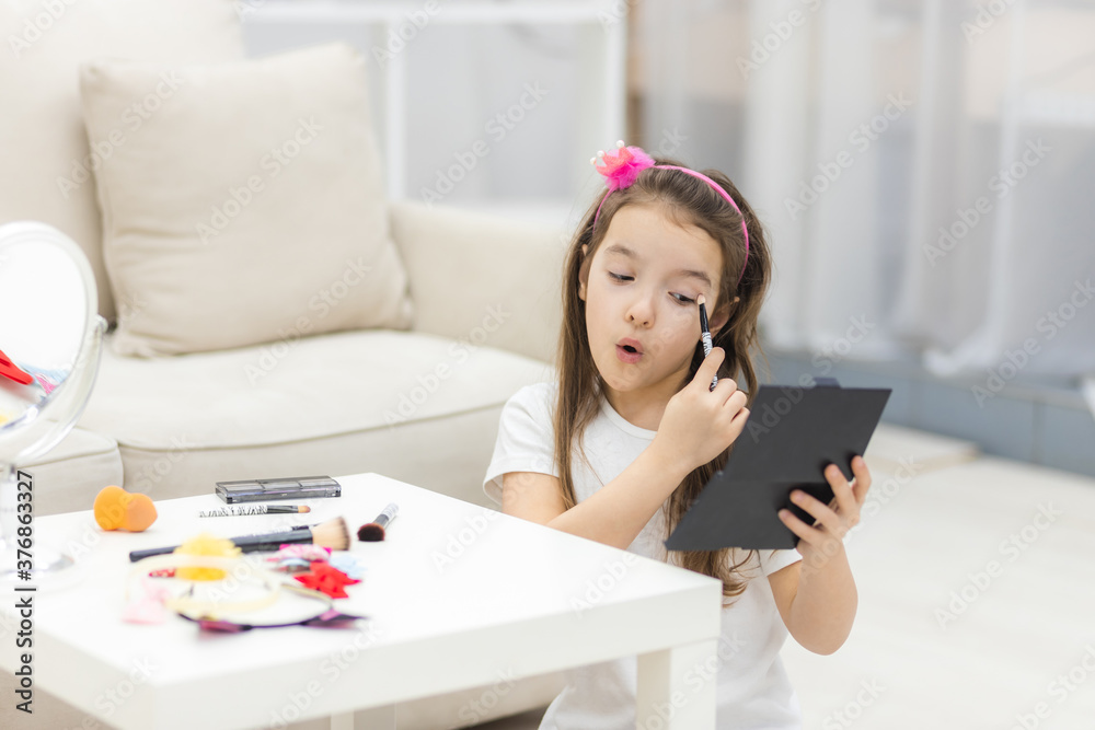 Photo of small girl painting her eyes looking in the mirror. Photo of small girl painting her eyes looking in the mirror.