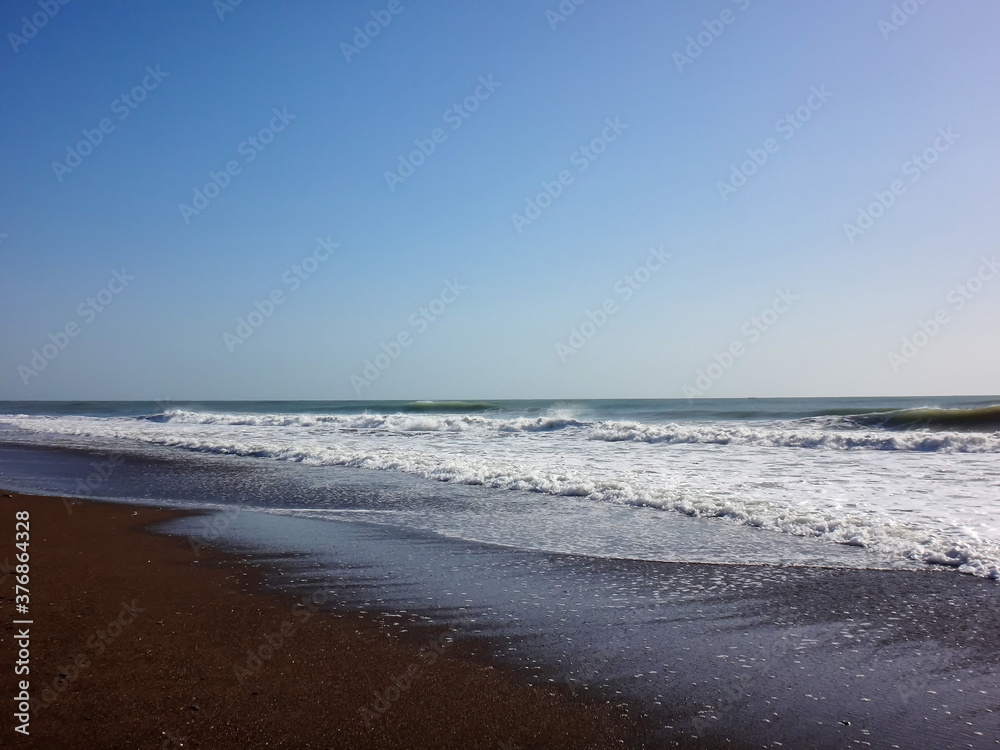 View from sand beach to water of sea and small waves in a nice day or evening with blues sky and bright sun. The concept of a holiday on the sea or ocean in the South.