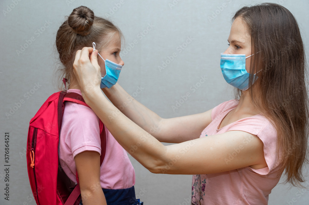 Portrait of a schoolgirl's daughter and mother in a medical mask. The mother puts a sterile medical mask on the child. Back to school. Get your child to school. Social distance and safety. Portrait of a schoolgirl's daughter and mother in a medical mask. The mother puts a sterile medical mask on the child. Back to school. Get your child to school. Social distance and safety.