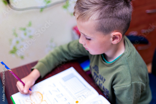 Close up side view of a schoolboy doing homework while sitting at a Desk at home. Reading books and completing lessons.