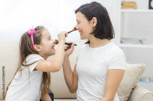 Photo of mother and little daughter smiling and holding cosmetics brushes.