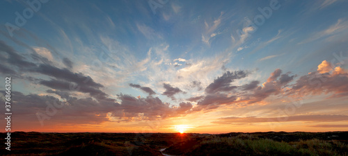 Panoramic view, beautiful sunset over the dunes, heavy clouds and sunset with sun rays, blue orange sky, sun in the middle, texel, Island © Sonja