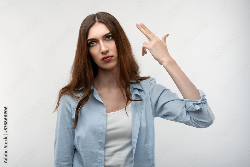 Unhappy Young woman tilts head, imitates gun shoot, has puzzled expression. Human emotions concept. Unhappy Young woman tilts head, imitates gun shoot, has puzzled expression. Human emotions concept.