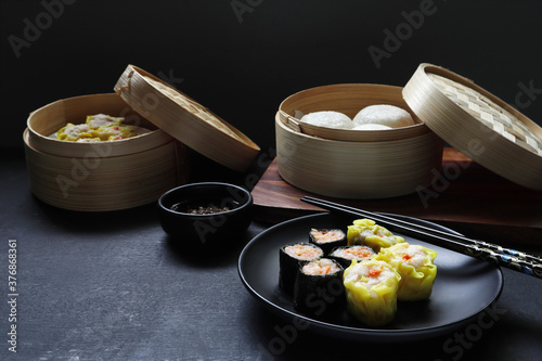 shrimp dumpling and seaweed minced pork rolls are in the black round dish on black wooden table with pork and egg creamy steam buns in the dim sum basket during lunch in the Chinese Conton restaurant photo