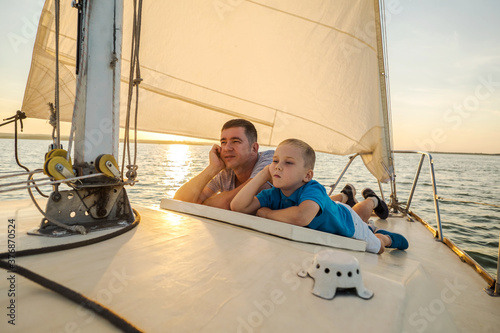 Happy traveler father and son enjoying sunset from deck of sailing boat moving in sea at evening time. Bonding Travel, Summer, Holidays, Journey, Trip, Lifestyle, Yachting concept. © Andrii IURLOV