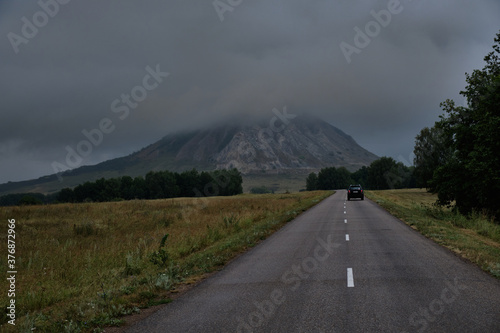 Car rides on an empty road to the mountain in cloudy weather