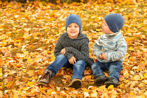 Children in yellow and gold autumn forest. Two little brothers on leafs in fall park. Family walk outdoor. Friendly relationship in family. Cozy and warm knitted sweaters