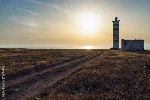 An old lighthouse on the edge of the sea, in the rays of the setting sun.
