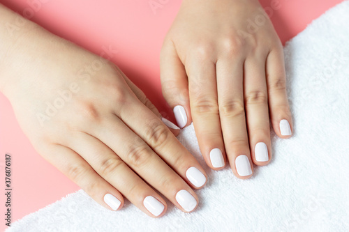Beautiful women s hands with white manicure on pink and white background