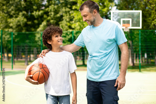 Mature dad embracing little boy who holding basket ball