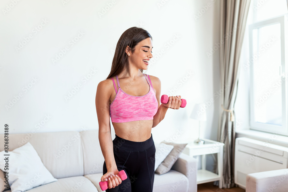 Woman exercising with dumbbells at home. Sporty beautiful woman exercising at home to stay fit. Young woman exercising at home in a living room. Fitness, workout, healthy living and diet concept.