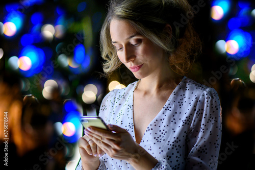 Woman with phone night portrait city lights bokeh. White dress lovely evening scenes
