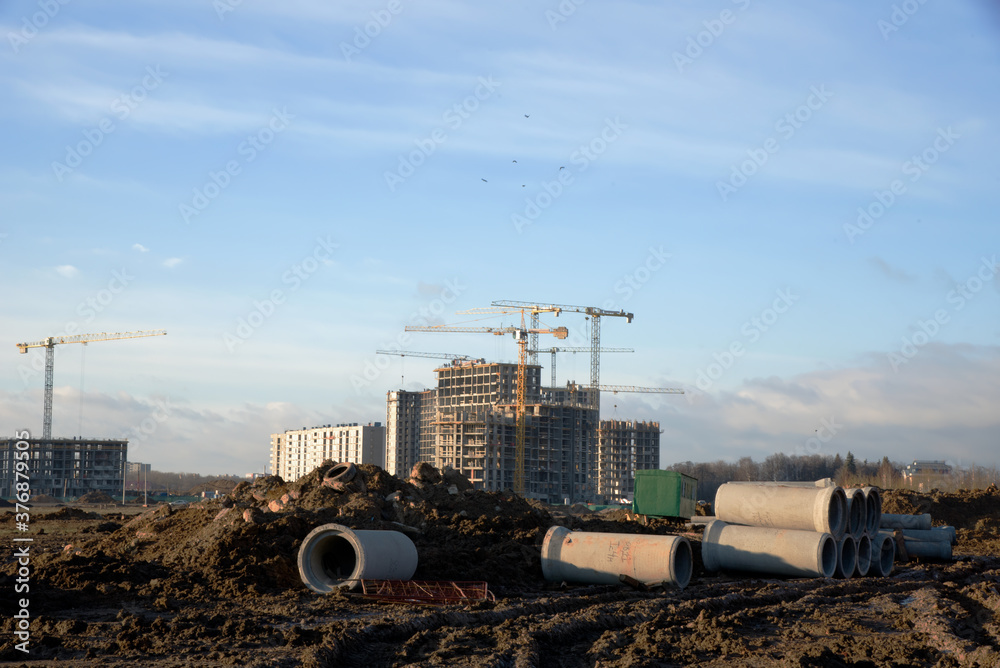 Tower cranes constructing a new residential build. Pouring concrete into formwork of building at construction site. Laying or replacement of underground storm sewer pipes. Concrete drainage pipe.