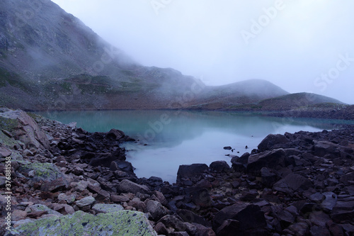 Alpine lake in the clouds. Alpine lake with rocky shores and emerald water in the clouds. Alpine lake Giybashkel (3240 meters above sea level), Caucasus. 