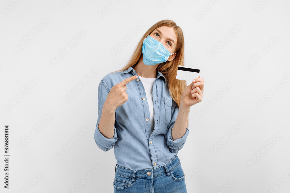 Pensive young woman in a medical protective mask on her face with a credit card in her hands on a white background Pensive young woman in a medical protective mask on her face with a credit card in her hands on a white background