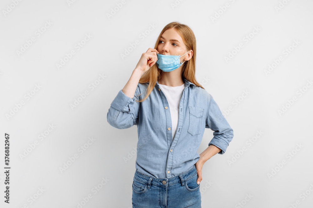 Pensive young woman in a medical protective mask on her face, on a white background