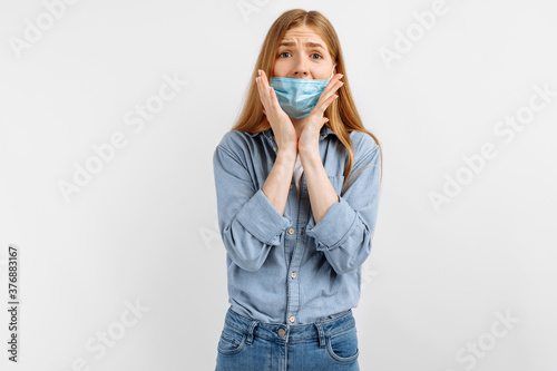 Shocked, surprised young woman in a medical mask on her face, surprised covers her mouth with her hand, on a white background