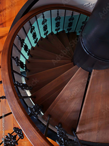 Vintage spiral staircase in brown wood with ornate black metal columns. Top view.