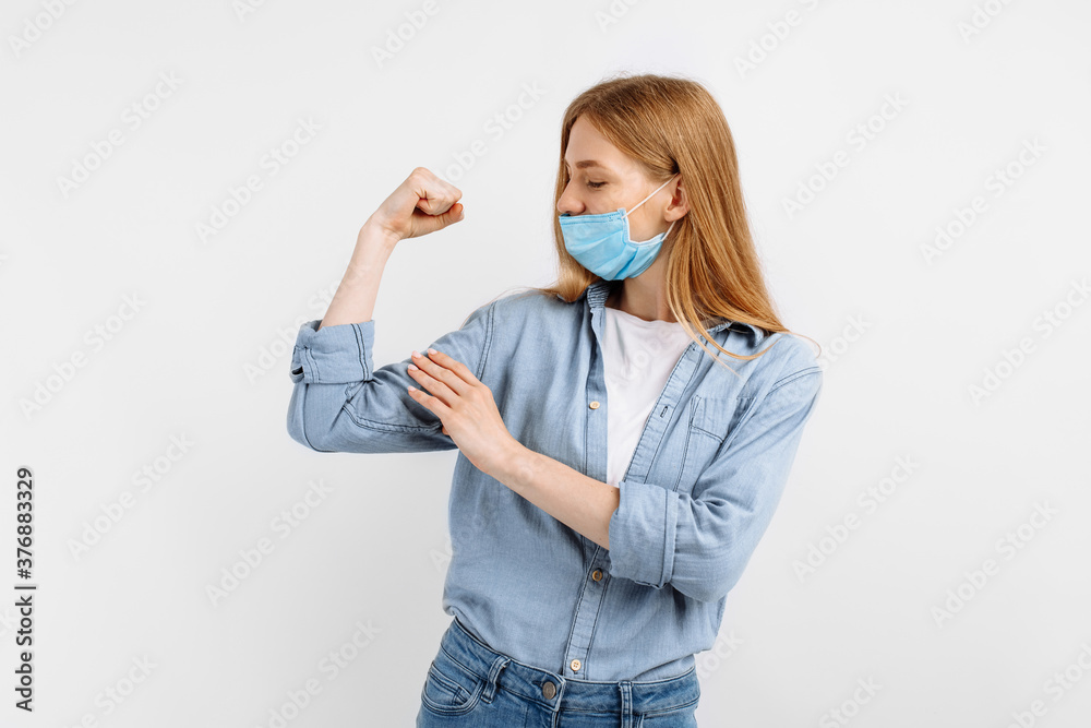 strong athletic young woman in a medical mask on her face, showing biceps on her arm, on an isolated white background strong athletic young woman in a medical mask on her face, showing biceps on her arm, on an isolated white background