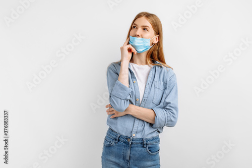 Pensive young woman in a medical mask on her face, on a white background