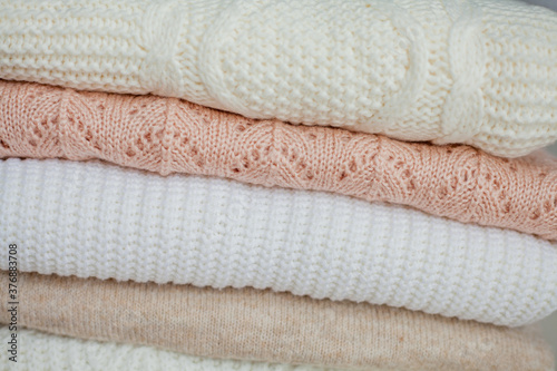 A stack of knitted sweaters, cotton. Women's sweaters lie on the ottoman. Cozy autumn clothes.