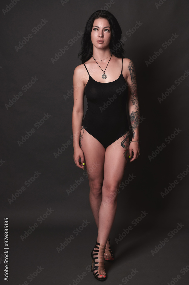 Tattooed brunette in black swimsuit on black background