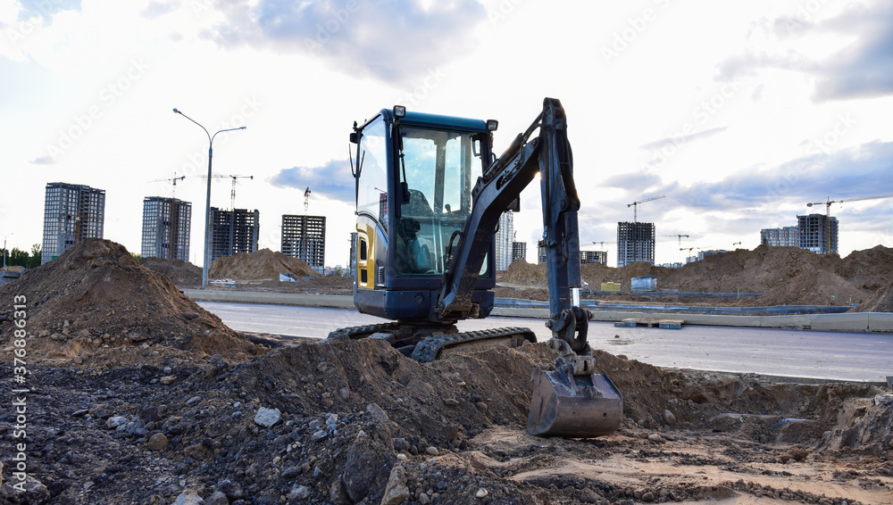 Mini excavator digg trench to lay cables concrete curbs and paving slabs at construction site. Backhoe on earthwork/roadworks Mini excavator digg trench to lay cables concrete curbs and paving slabs at construction site. Backhoe on earthwork/roadworks