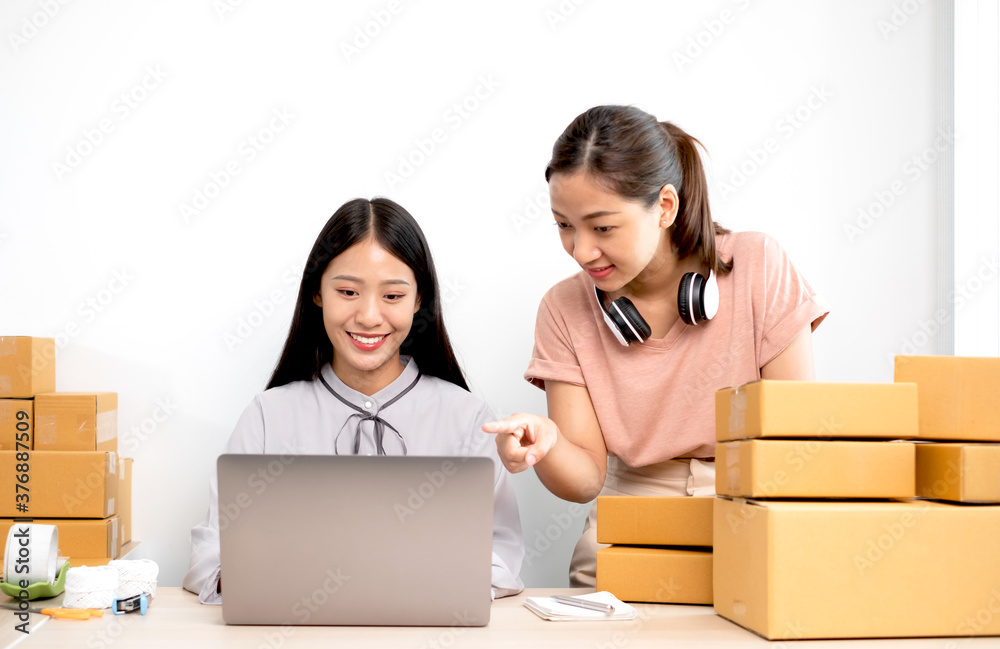Asian woman business two people owner with many parcel boxes on the table happy online sales job, use your laptop, get an order from customers, take notes, and make arrangements for delivery by post Asian woman business two people owner with many parcel boxes on the table happy online sales job, use your laptop, get an order from customers, take notes, and make arrangements for delivery by post