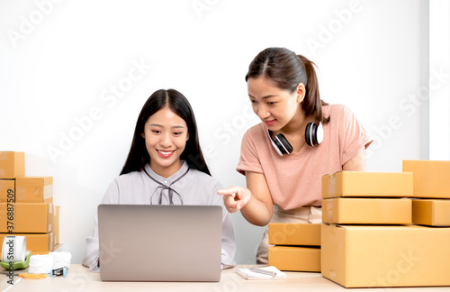 Asian woman business two people owner with many parcel boxes on the table happy online sales job, use your laptop, get an order from customers, take notes, and make arrangements for delivery by post