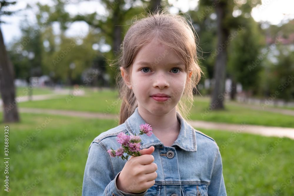 little cute girl holding a bouquet of clover flowers in her hands, street portrait in the park little cute girl holding a bouquet of clover flowers in her hands, street portrait in the park