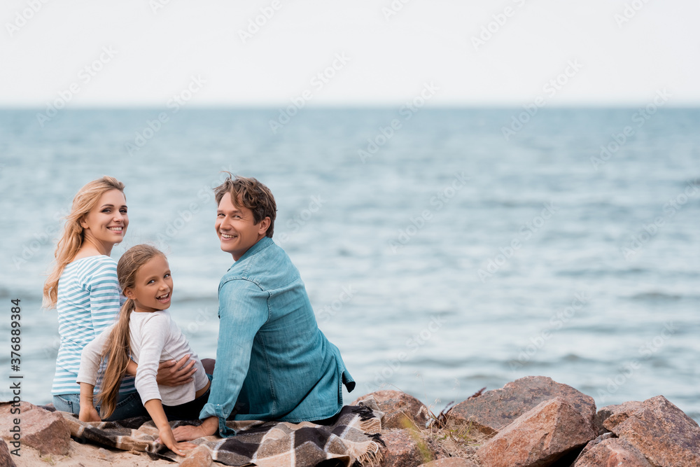 Selective focus of family with kid looking at camera on seaside Selective focus of family with kid looking at camera on seaside
