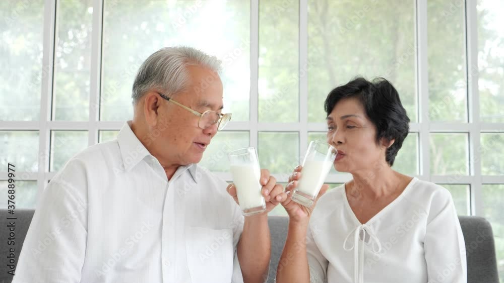 Portrait Asian senior elderly couple look at camera and drinking milk on the sofa at home. Senior healthy concept. Portrait Asian senior elderly couple look at camera and drinking milk on the sofa at home. Senior healthy concept.