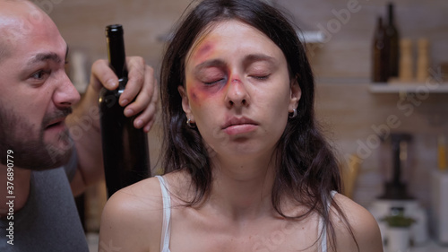 Bruised woman looking at the room while drunk husband screams in the background. Traumatised abused terrified helpless, vulnerable, beaten wife suffering injury from alcoholic violent brutal man
