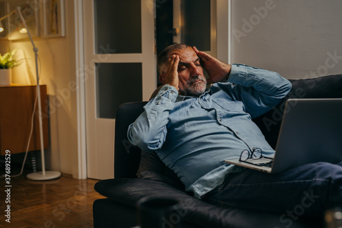 middle aged man sitting sofa having headache while using laptop computer at home © cherryandbees