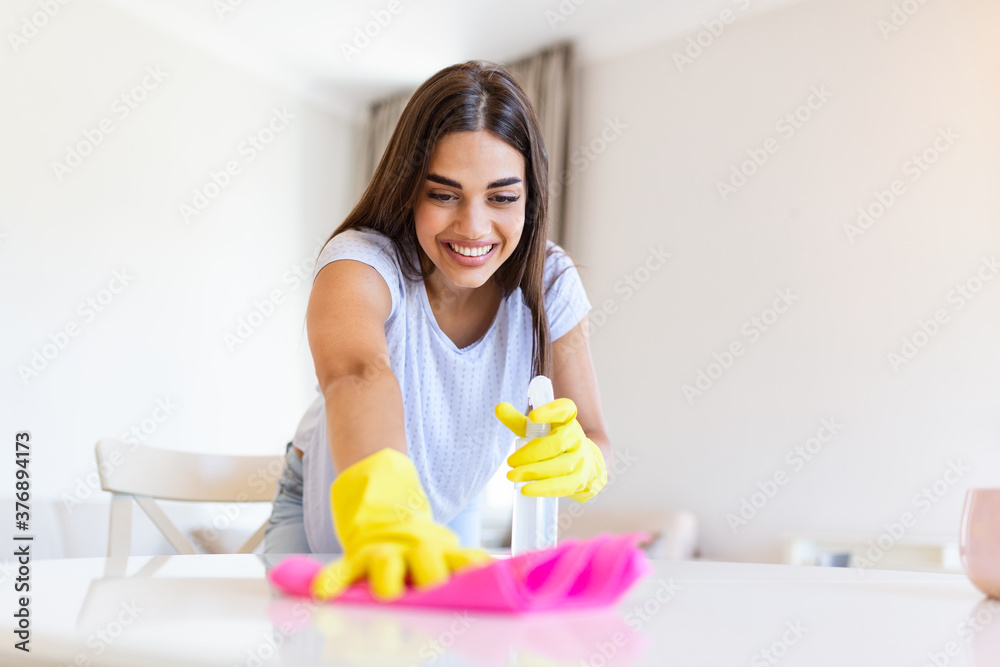 Beautiful young woman makes cleaning the house. Girl rubs dust. Smiling woman wearing rubber protective yellow gloves cleaning with rag and spray bottle detergent. Home, housekeeping concept. Beautiful young woman makes cleaning the house. Girl rubs dust. Smiling woman wearing rubber protective yellow gloves cleaning with rag and spray bottle detergent. Home, housekeeping concept.