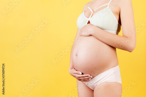 Cropped image of pregnant woman hugging her abdomen. Mother is wearing colorful underwear at yellow background. Future parent is expecting her child. Copy space