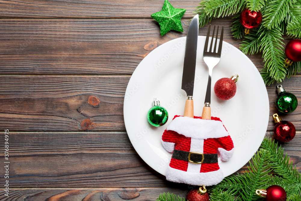 Top view of fork, knife and plate surrounded with fir tree and Christmas decoratoins on wooden background. New Year Eve and holiday dinner concept Top view of fork, knife and plate surrounded with fir tree and Christmas decoratoins on wooden background. New Year Eve and holiday dinner concept